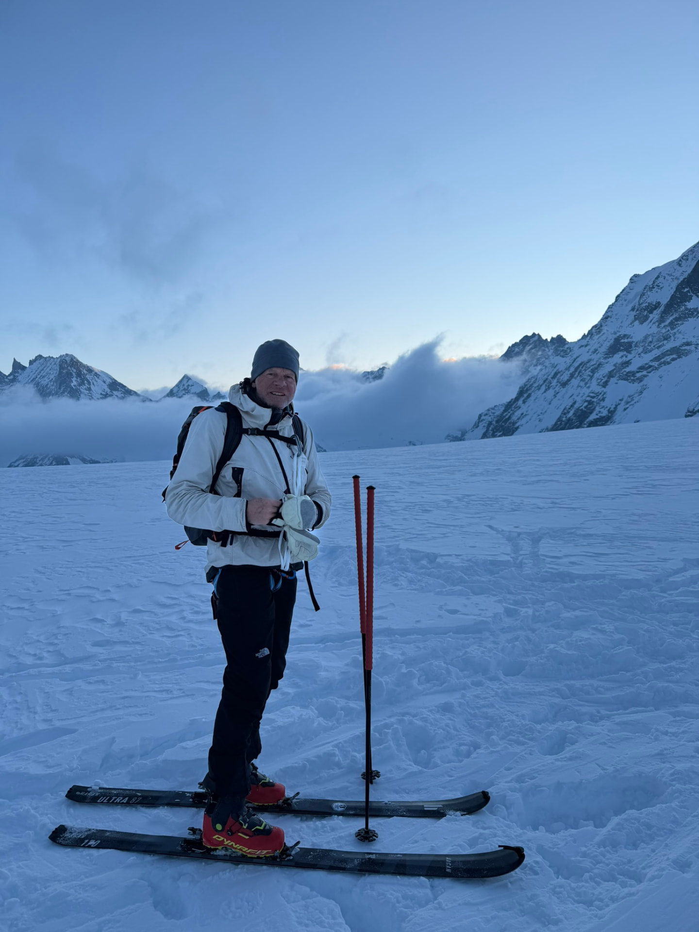 Skidåkare på en glaciär i gryningsljus med toppar över molnhavet